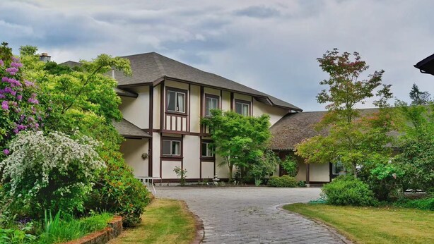 A two-story building with a traditional architectural style, a paved driveway, and lush greenery surrounding the property.