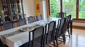 A dining area with a long table, black mesh chairs, and a traditional cabinet with glass doors.