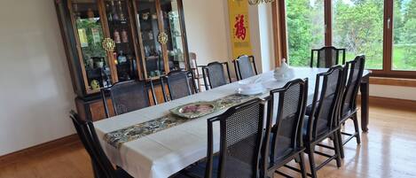 A dining area with a long table, black mesh chairs, and a traditional cabinet with glass doors.