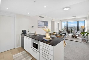 A modern kitchen with a dining area, large windows, and a view of the city. - Serene Coastal Apartment w/Free Parking+Pool+Gym (Broadbeach)