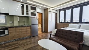Ein modernes Hotelzimmer mit einer Küchenzeile, einem Bett mit brauner Kopfteil und Blick auf die Stadt durch große Fenster.
