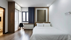 Quarto de hotel com cama, escrivaninha, cadeira, janela com cortinas e televisão.