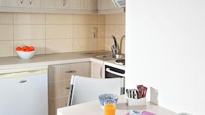 A modern kitchen with a dining area, including a table with a plate of food, a mug, and a bowl of fruit. - Fodele Beach Front Apts. (Malevizi)