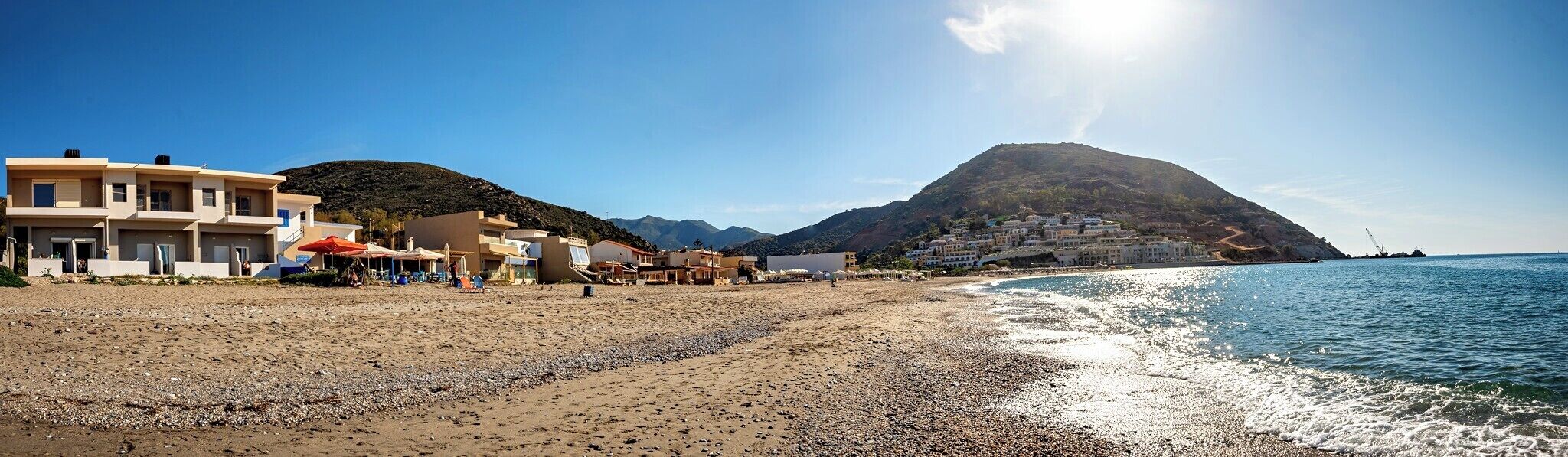 A beach with buildings, a mountain, and clear skies.