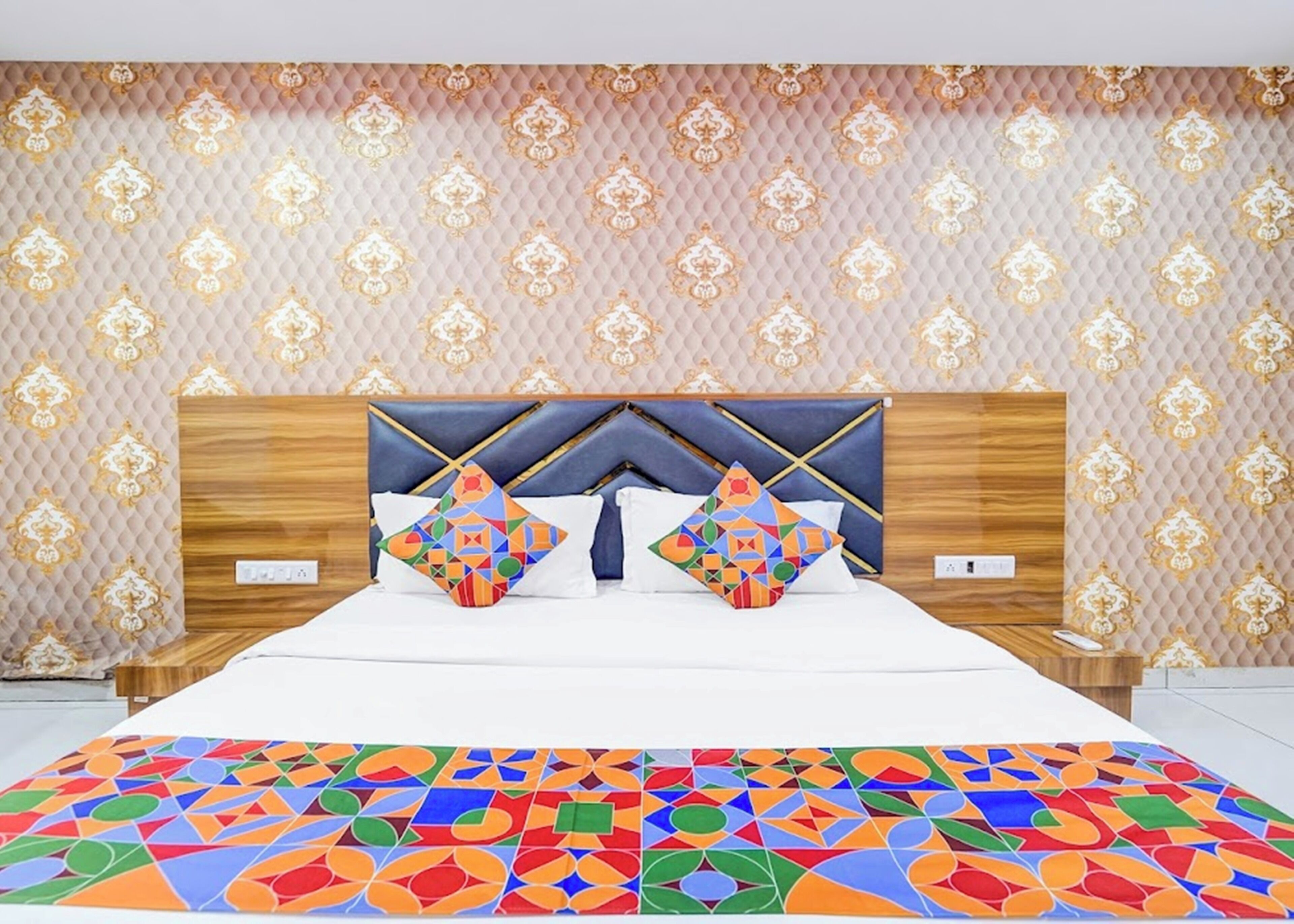 A hotel room with a large bed, a headboard with a geometric pattern, and a patterned wall.