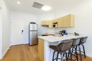 A compact kitchen with a refrigerator, microwave, and a small island with bar stools. - Resort Escape: King Bed, Pool & Balcony (Darwin City)