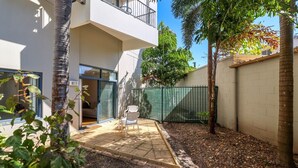 Un edificio residencial con un patio, puerta corrediza de vidrio, cerca verde y un pequeño jardín.