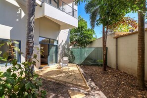 Un edificio residencial con un patio, puerta corrediza de vidrio, cerca verde y un pequeño jardín.