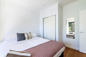 A bedroom with a bed, a bedside table, a window, and a door. - Resort Escape: King Bed, Pool & Balcony (Darwin City)