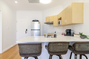 A modern kitchen with a central island, wooden cabinets, a stainless steel refrigerator, and a microwave. - Resort Escape: King Bed, Pool & Balcony (Darwin City)