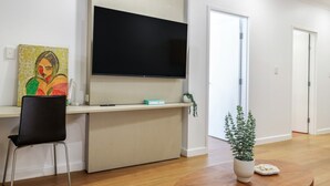 Una sala de estar moderna con una televisión de pantalla plana, un cuadro, una silla, una mesita con una planta y una puerta que da a otra habitación.