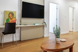 A modern living room with a flat-screen TV, a painting, a chair, a small table with a plant, and a door leading to another room. - Resort Escape: King Bed, Pool & Balcony (Darwin City)