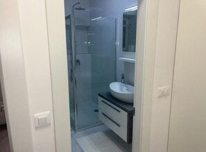 Une salle de bain moderne avec une douche à parois de verre, un lavabo blanc et un miroir au-dessus du meuble-lavabo.