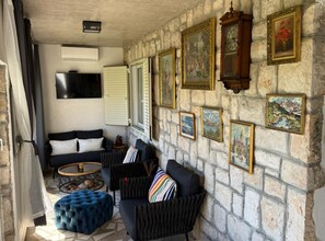 A room with a stone wall, a sofa, a chair, a round coffee table, and a television. - Apartment La Mar (Lastovo)