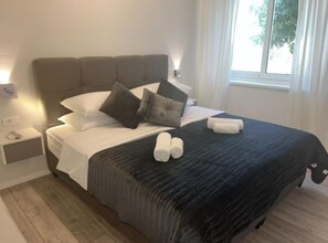 A neatly made bed with pillows, a bedside table with a lamp, and a window with curtains. - Apartment La Mar (Lastovo)