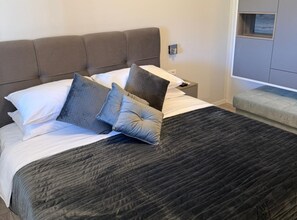 Un lit bien fait, avec une couverture sombre, une tête de lit et plusieurs oreillers.