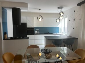A modern kitchen with white cabinets, a black range hood, and a blue backsplash. - Apartment La Mar (Lastovo)
