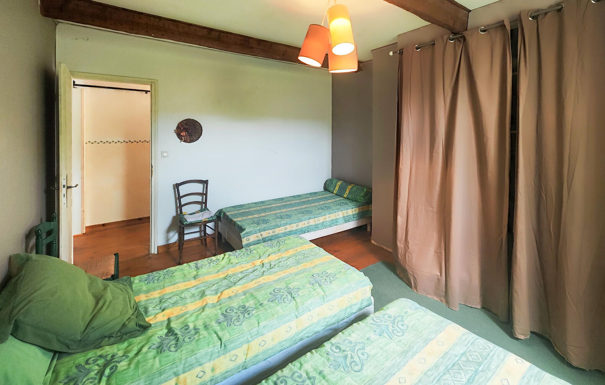 A room with two beds, a chair, a door, and a hanging light fixture.