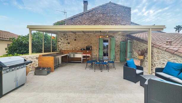 An outdoor patio with a stone wall, a grill, a table with chairs, and a covered seating area. - Gorgeous apartment in Cessenon-Sur-Orb with WiFi (Cessenon-Sur-Orb)