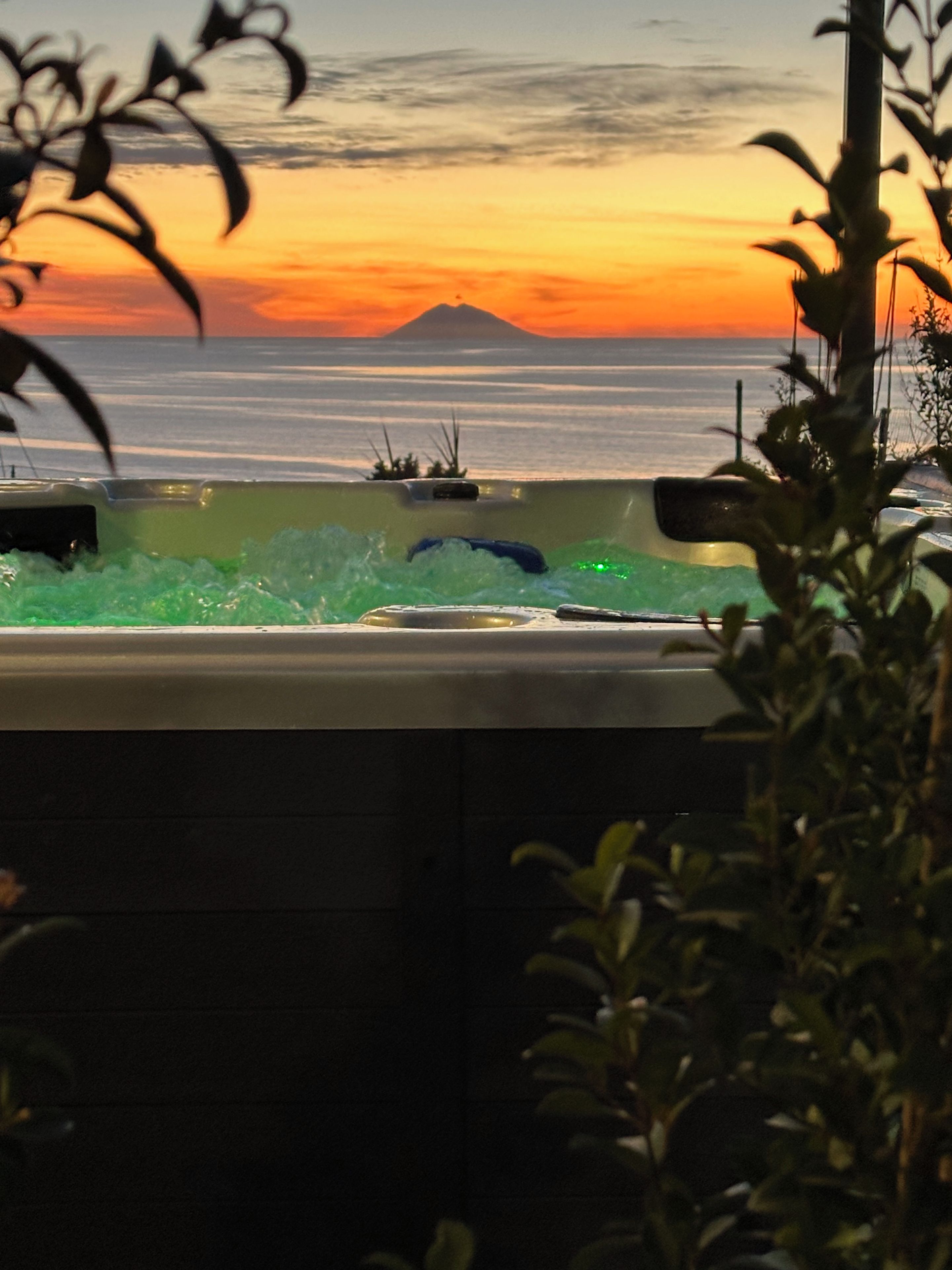 Un bain à remous avec vue sur un coucher de soleil et une montagne au loin.