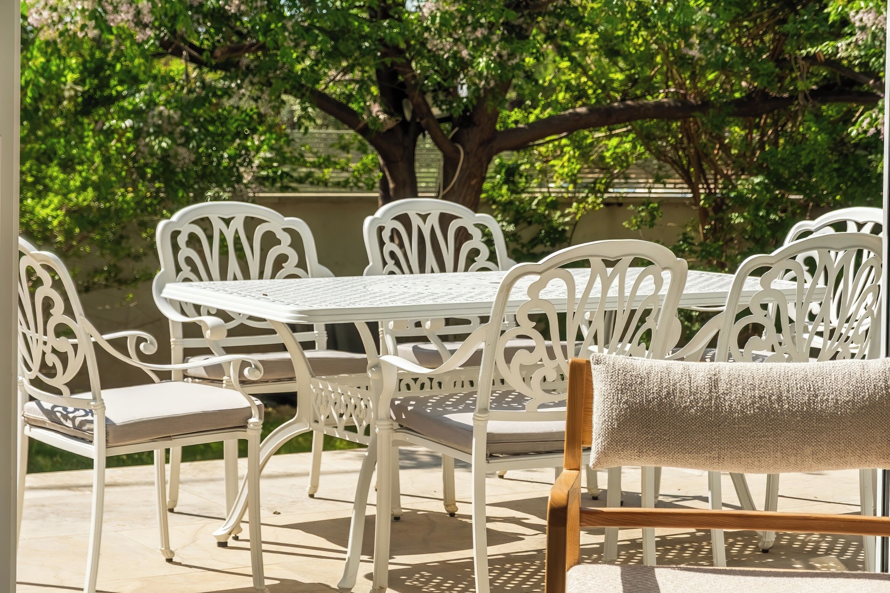A white outdoor dining set with chairs and a table, surrounded by greenery.