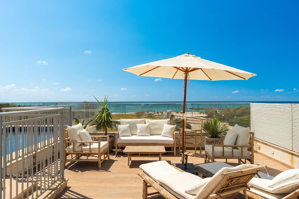 Terraza en la azotea con piscina, asientos blancos acolchados y una sombrilla grande.