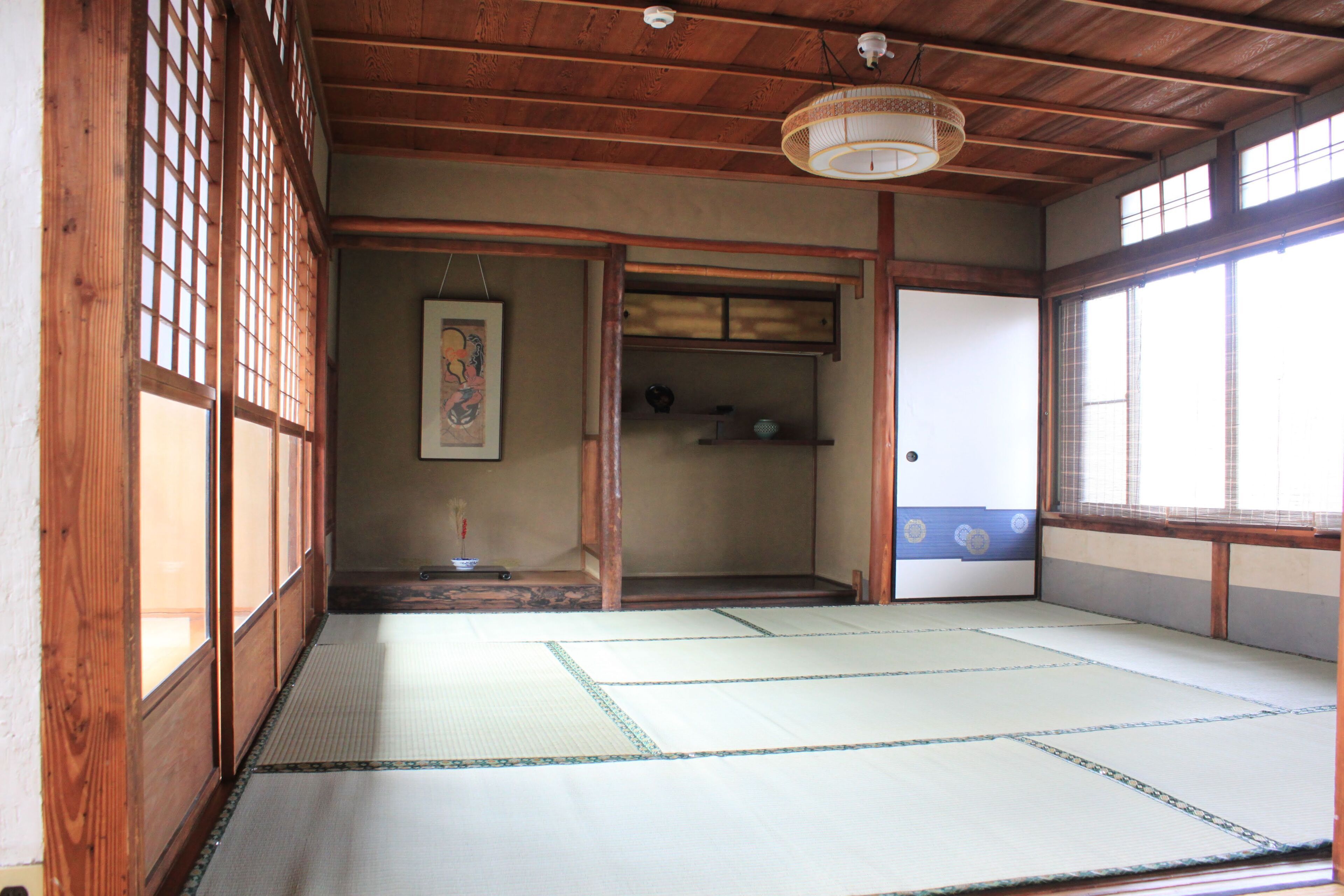 A traditional Japanese room with tatami flooring, wooden sliding doors, and a hanging light fixture.