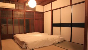 Una habitación japonesa tradicional con suelo de tatami, futón, puertas correderas y un ventilador de techo.