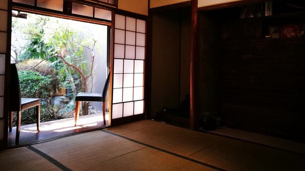 Una habitación japonesa tradicional con suelo de tatami, puertas correderas y vistas a zonas verdes.