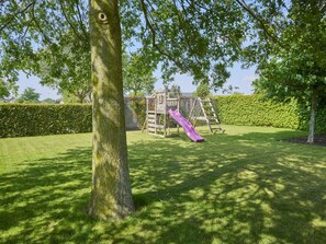 Une aire de jeux avec un toboggan et une structure d’escalade, entourée d’une pelouse bien entretenue et d’une haie.