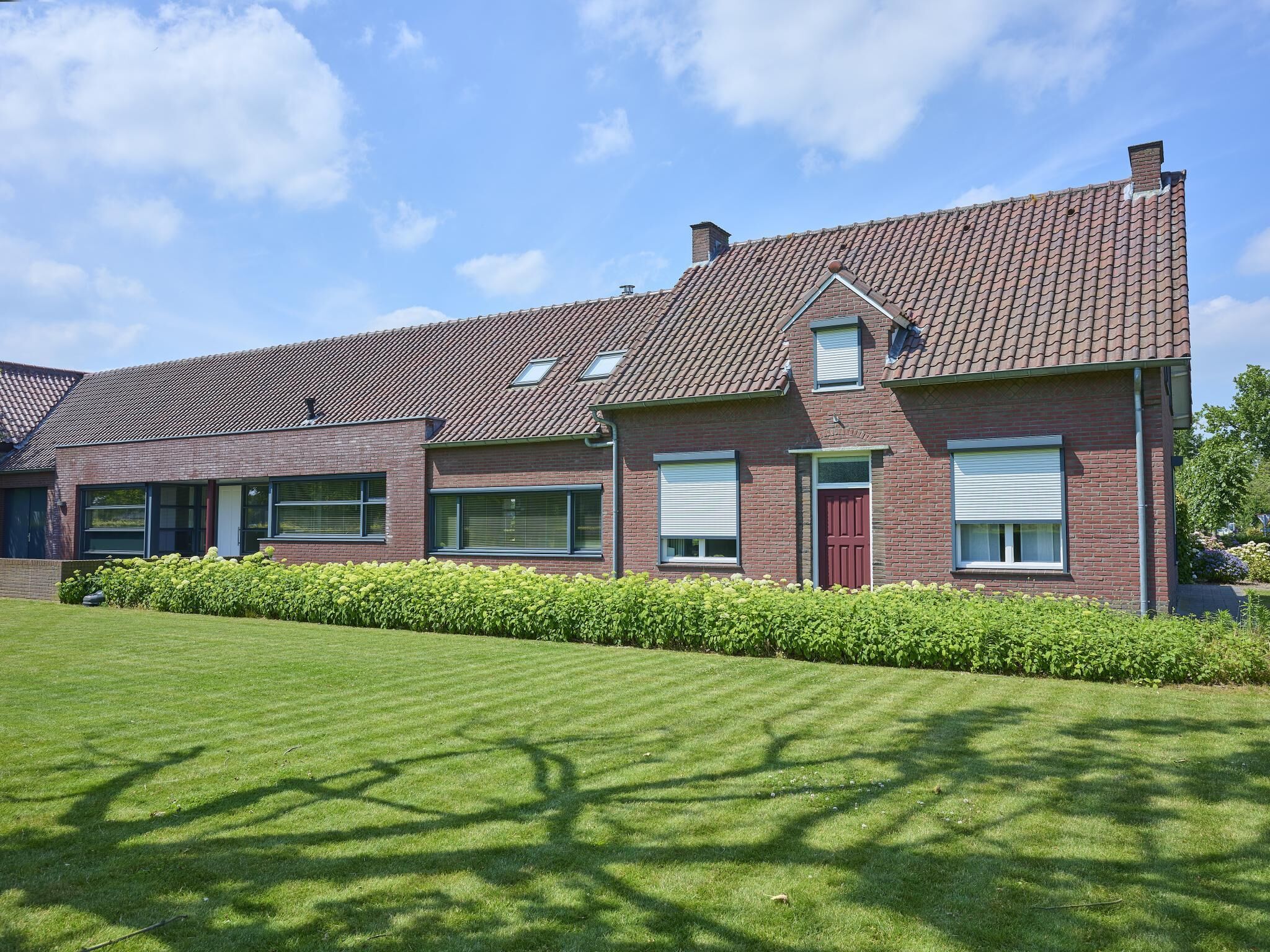 A two-story brick house with a tiled roof, large windows, and a well-maintained lawn.
