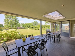 A patio with a table and chairs, a grill, and a view of a garden.