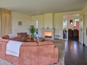 A living room with a sofa, a fireplace, a dining area, and a kitchen visible through an open door.