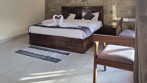 A bedroom with a wooden ceiling, a brick wall, a bed with white linens, two bedside lamps, and a wooden chair.