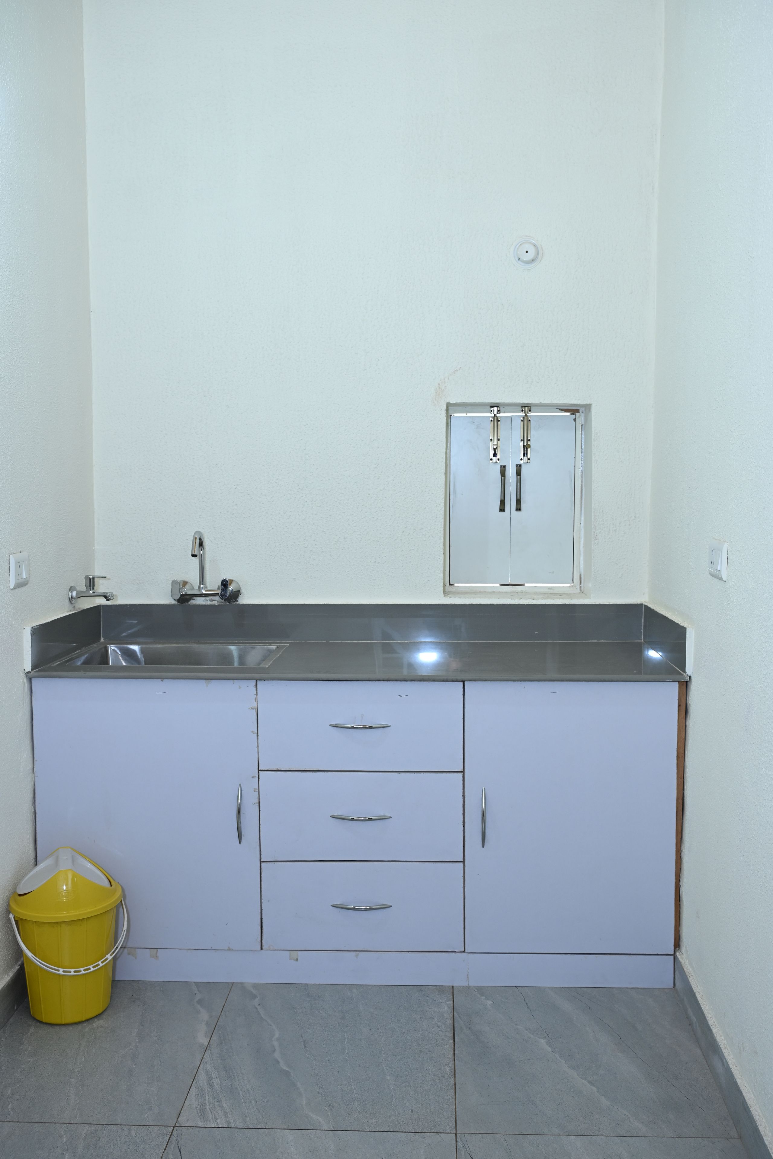 A kitchen with a sink, cabinets, and a yellow bucket.