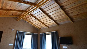 A room with a sloped wooden ceiling, two windows with curtains, and a flat-screen TV mounted on the wall.