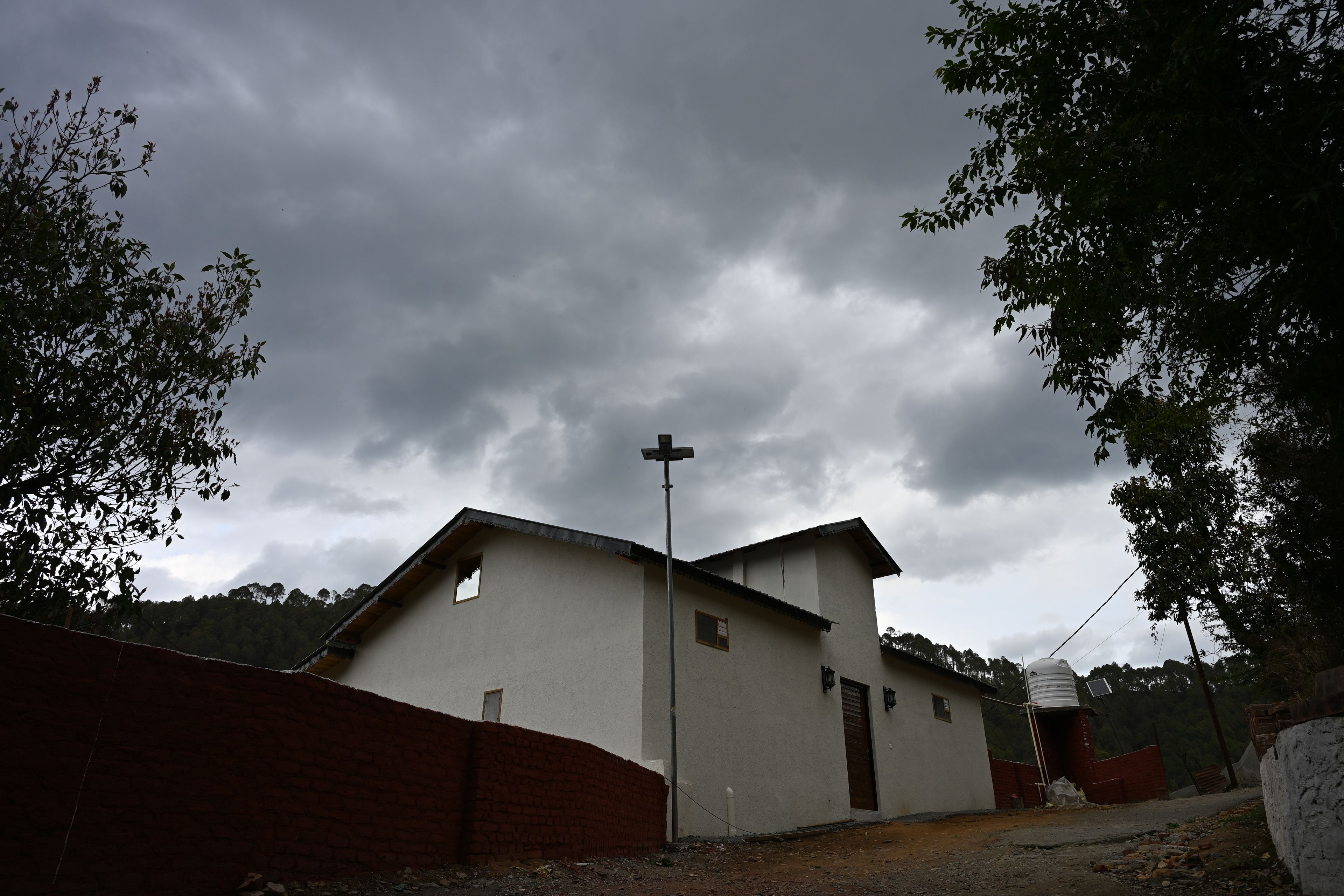 A building with a flat roof, a cross on top, and a small window.