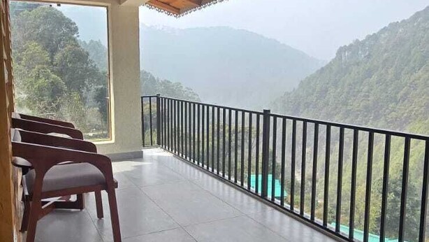 A balcony with a view of green hills, wooden ceiling beams, and a black railing.