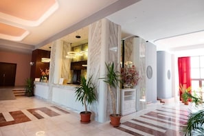 A hotel lobby with marble columns, a reception desk, potted plants, and modern lighting fixtures. - Hotel Ambasador Mamaia (Constanța)