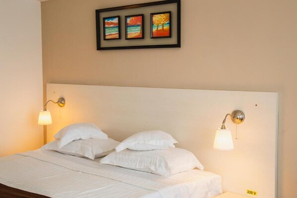 A bed with white bedding, two wall-mounted lamps, and three framed paintings above it. - Hotel Ambasador Mamaia (Constanța)