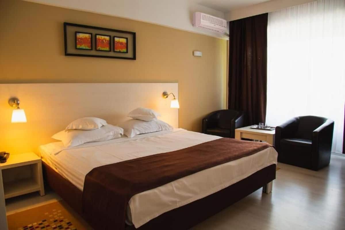 Habitación de hotel con cama, dos lámparas de noche, un escritorio con silla y una ventana con cortinas.