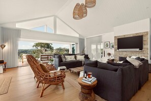 A spacious living area with a large sofa, a wicker chair, and a television mounted on the wall. - Fairview Rise | Main Residence (Hahndorf)