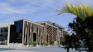Un bâtiment moderne doté d’une façade originale, caractérisée par des motifs verticaux et en forme de nid d’abeilles, ainsi qu’un ciel dégagé et un espace piscine.