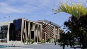 A modern building with a unique facade featuring vertical and honeycomb-like patterns, a clear sky, and a pool area.