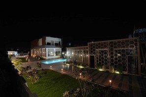 A modern building with a swimming pool, a hexagonal glass structure, and a well-lit outdoor area.