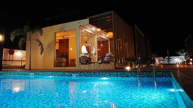 Un bâtiment moderne doté d’une piscine, d’un espace repas avec des chaises et d’une entrée bien visible.