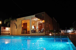 A modern building with a pool, a dining area with chairs, and a visible entrance.