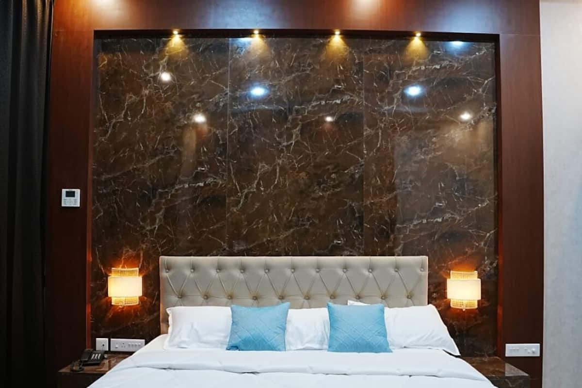 A modern hotel room with a large bed, marble headboard, and wall-mounted reading lights.