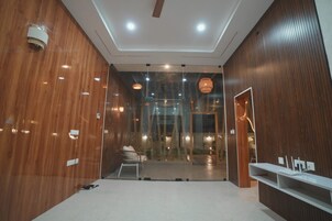 A modern interior with wooden paneling, recessed ceiling lights, a seating area with a chair and a small table, and a glass partition.