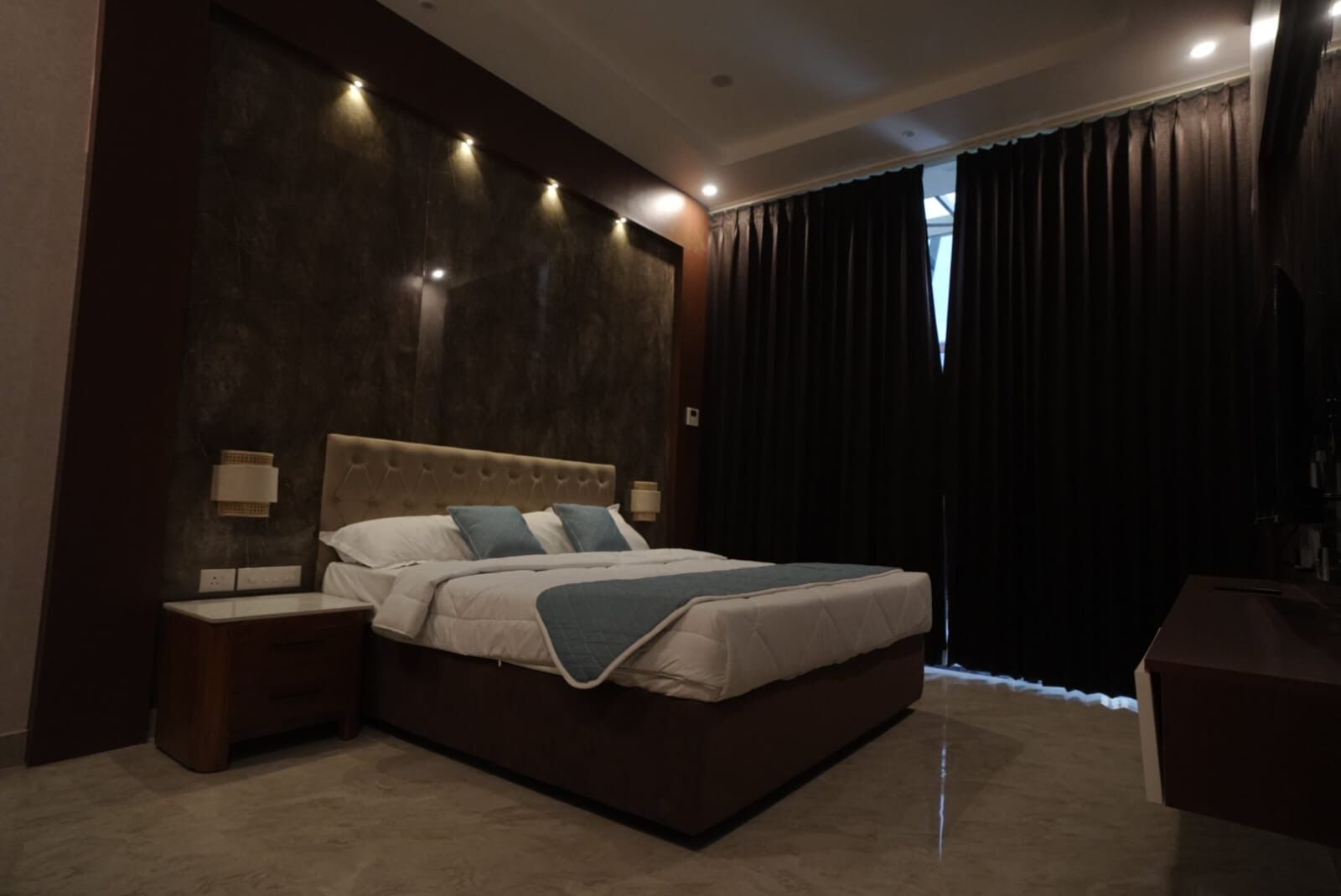 Une chambre moderne avec un grand lit, des tables de chevet et une vue sur l’extérieur à travers les rideaux.